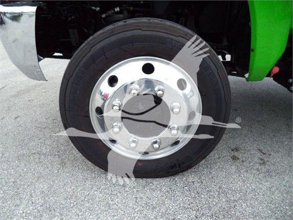 Truck front wheel close-up showing polished chrome rim with lug nuts and black tire; partial green body panel visible.