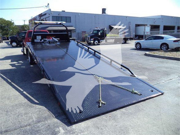 Ram 5500 tow truck flatbed showing large diamond plate steel bed and ramp with winches and rear hitch, in a dealership lot.