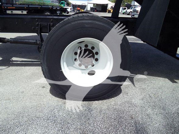 Wheel and tire of a heavy-duty truck trailer showing a white steel rim and black tire. Partial chassis visible in background.