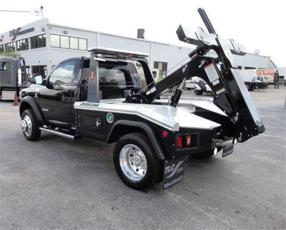 Tow truck setup on a black 2024 Ram 4500 HD SLT with a rear bed hydraulic tow boom and folded bed, showing chrome wheels and a small green circular badge on the door.