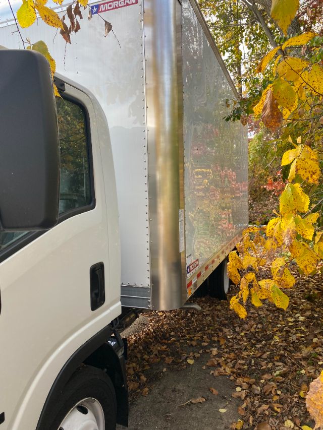 Isuzu NRR gas cab chassis truck with a large aluminum box cargo area; side view showing cab, windshield, and box panels with rivets; fall leaves around.