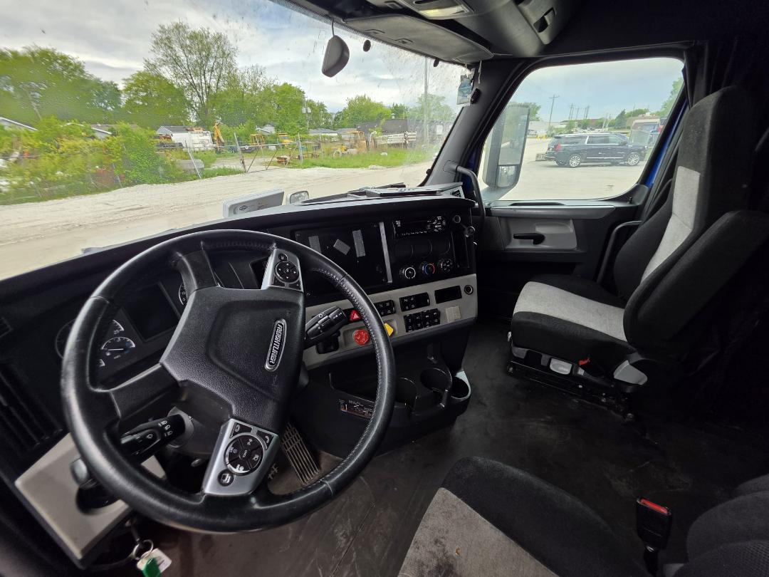 Cab interior of 2018 Freightliner Cascadia truck showing steering wheel, dashboard with gauges, center console, and driver seat.