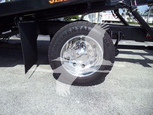 Wheel well and tire on a tow truck chassis showing chrome wheel and partial black frame with hydraulic components.