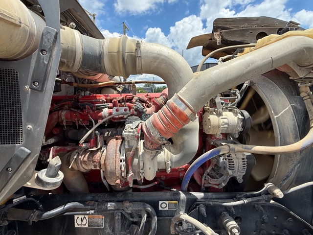 Kenworth W900 engine bay showing large intake piping, red engine block, alternator, and various hoses.