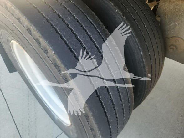 Trailer axle with dual tires; no readable labels visible due to watermark; close-up of wheel and tread shows two tires and a steel hubcap.