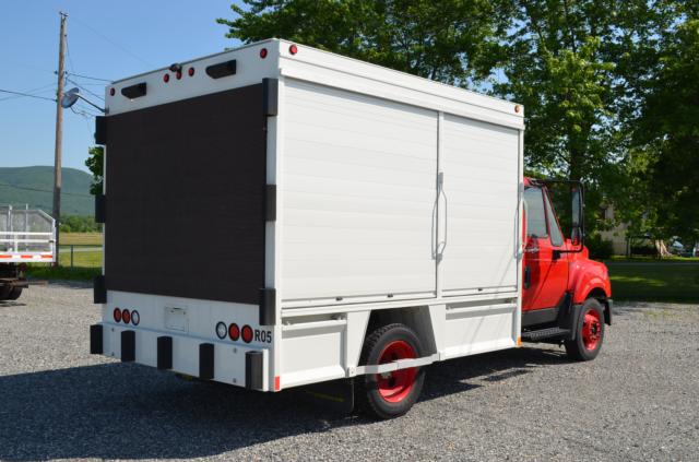 2013 International TerraStar beverage truck with white cargo box and red cab, side doors, rear roll-up doors, in a gravel lot.