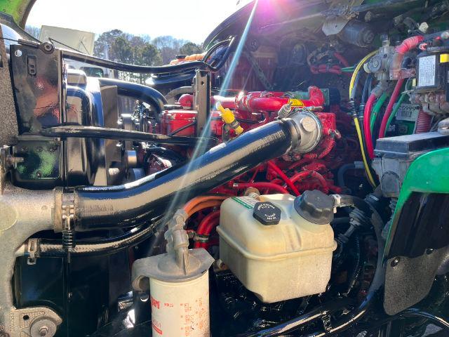 Truck engine bay of a 2016 Freightliner M2 106 showing red engine components, black radiator hose, coolant reservoir and power steering reservoir.