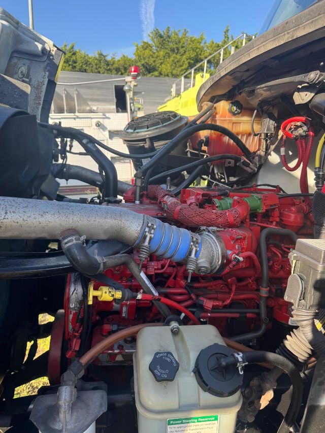 Freightliner 114SD engine bay with red engine, blue intercooler hose, coolant reservoir, and various hoses and wires visible.