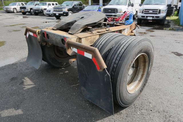 Dolly trailer rear view showing dual tires, fenders, and fifth-wheel coupling with hoses in a used equipment lot.