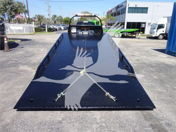 Ram 5500 flatbed with a large black steel ramp, chains secured, in a dealership lot.