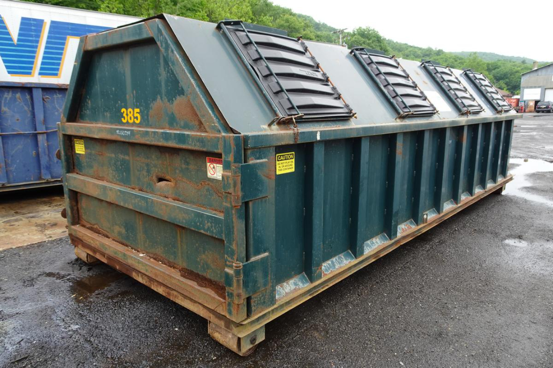 Wastequip 20 yd dumpster container in green with rust and warning labels, side vents along top, on wooden pallet base.