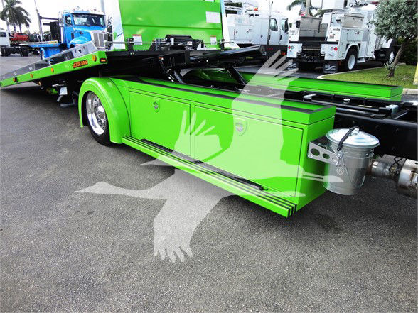 Green Peterbilt 337 tow truck chassis with side storage compartments and hydraulic lift platform. Visible metal fuel/air tanks and utility components along the frame.