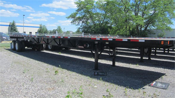 Flatbed trailer with extendable all-steel frame, long extendable sections, and dual rear axles; visible support legs down in gravel lot.