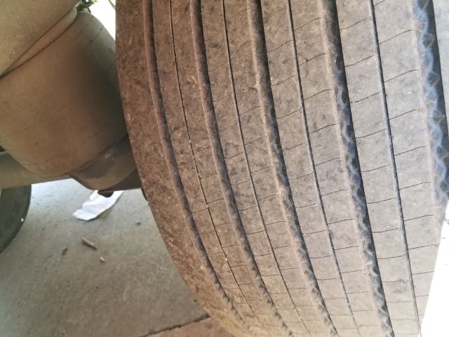 Trailer tire tread close-up with suspension and exhaust visible; no readable textual labels.