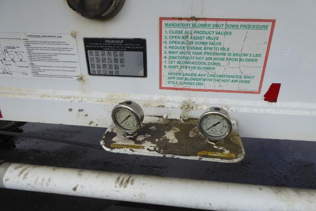 Fruehauf pneumatic dry bulk trailer rear with two pressure gauges and safety instruction label. Visible text includes 'MANDATORY BLOWER SHUT DOWN PROCEDURE' and steps 1-8, plus small plaque with FRUEHAUF information.
