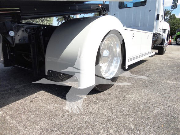 Truck front wheel and fender area of a 2022 Hino 268A tow truck showing white body, large chrome wheel, and black chassis