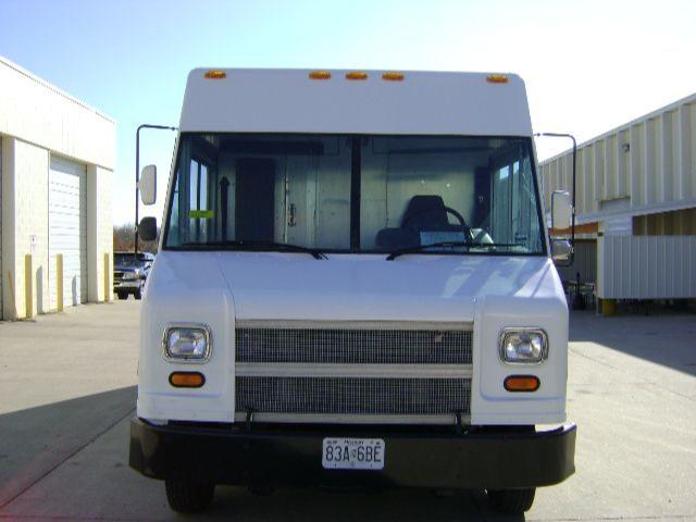 Front view of a white Freightliner MT45 step van with a large grille, square headlights, and orange indicator lights; windshield and side mirrors visible.