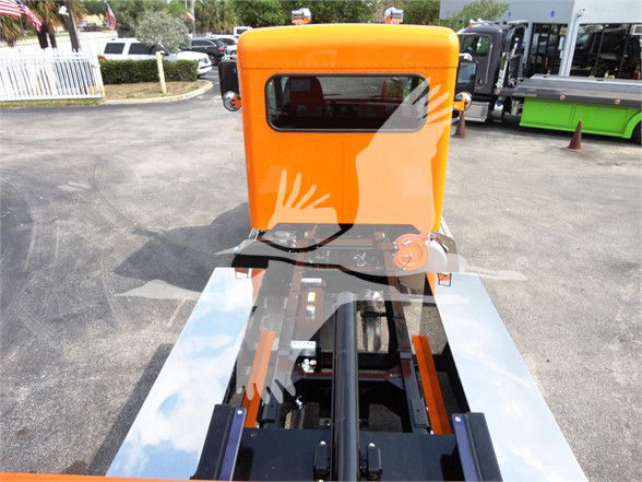 Front view of an empty orange Peterbilt truck cab with a forklift-like chassis behind it. Visible are the orange cab, black chassis, chrome rails, and a window reflecting the sky.