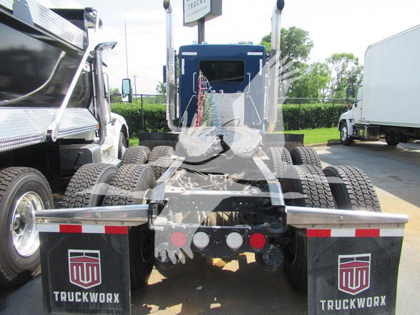Kenworth W900L chassis rear view showing dual rear axles and fifth wheel, with TruckWorx mudflaps and license plate area visible.