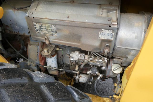 Tractor-style engine bay of Bomag BW212D-2 compact roller showing engine components, filters, hoses, and metal housing.