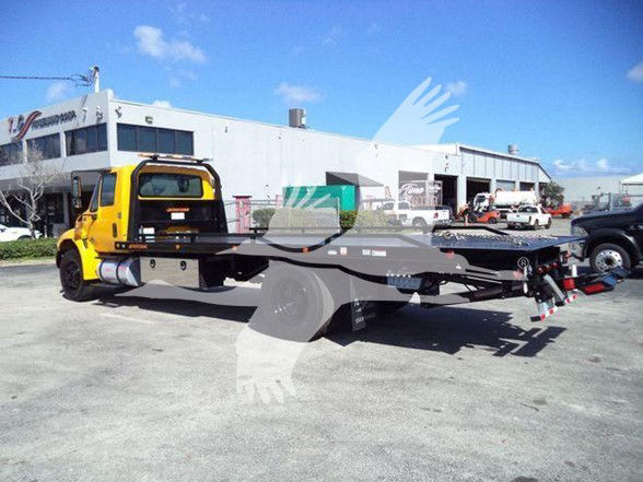 Tow truck flatbed chassis in an outdoor lot with a yellow cab, multiple buildings in background.