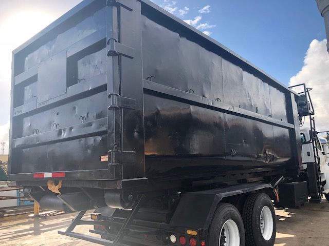 Rear/side view of a black dump truck with large dump bed, dual rear wheels, and a hydraulic tail gate. No legible text visible on decals.