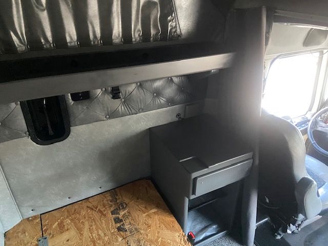 Cab interior of a 2015 Mack CXU613 truck showing sleeper area with diamond-tufted upholstery, grey panels, and a small storage drawer unit.