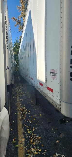 Trailer side showing white Wabash dry van trailer with reflective red markings and logo near the corner stake.