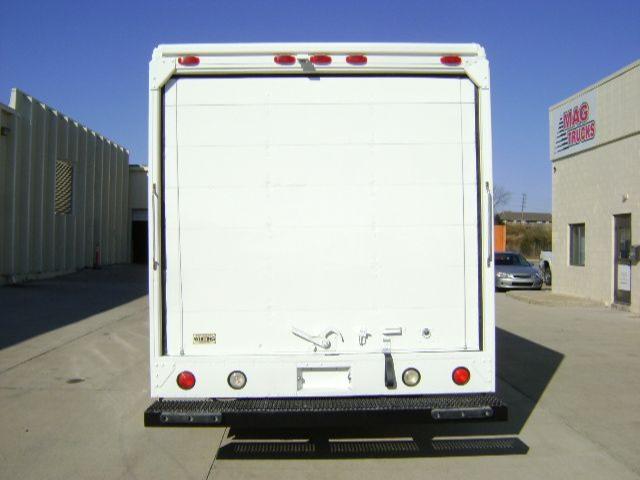 Back of a white 2008 Freightliner MT45 step van with rear doors, taillights, bumper, and mudflap. MAG B Trucks sign visible on right building.