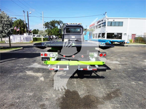 Rear view of a 2022 Peterbilt 337 tow truck with a bright-green rear bumper and bed, license plate area, lights, and towing apparatus visible.