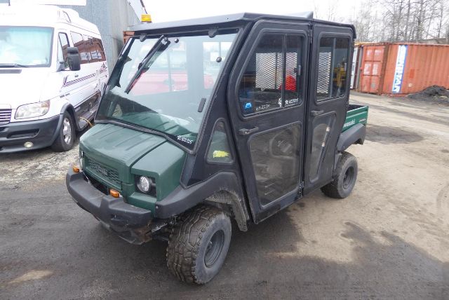Kawasaki KAF950G utility truck with enclosed cab and mesh doors, green body, black frame, compact tires, side cargo bed; visible front bumper and windshield; lettering stickers on door.