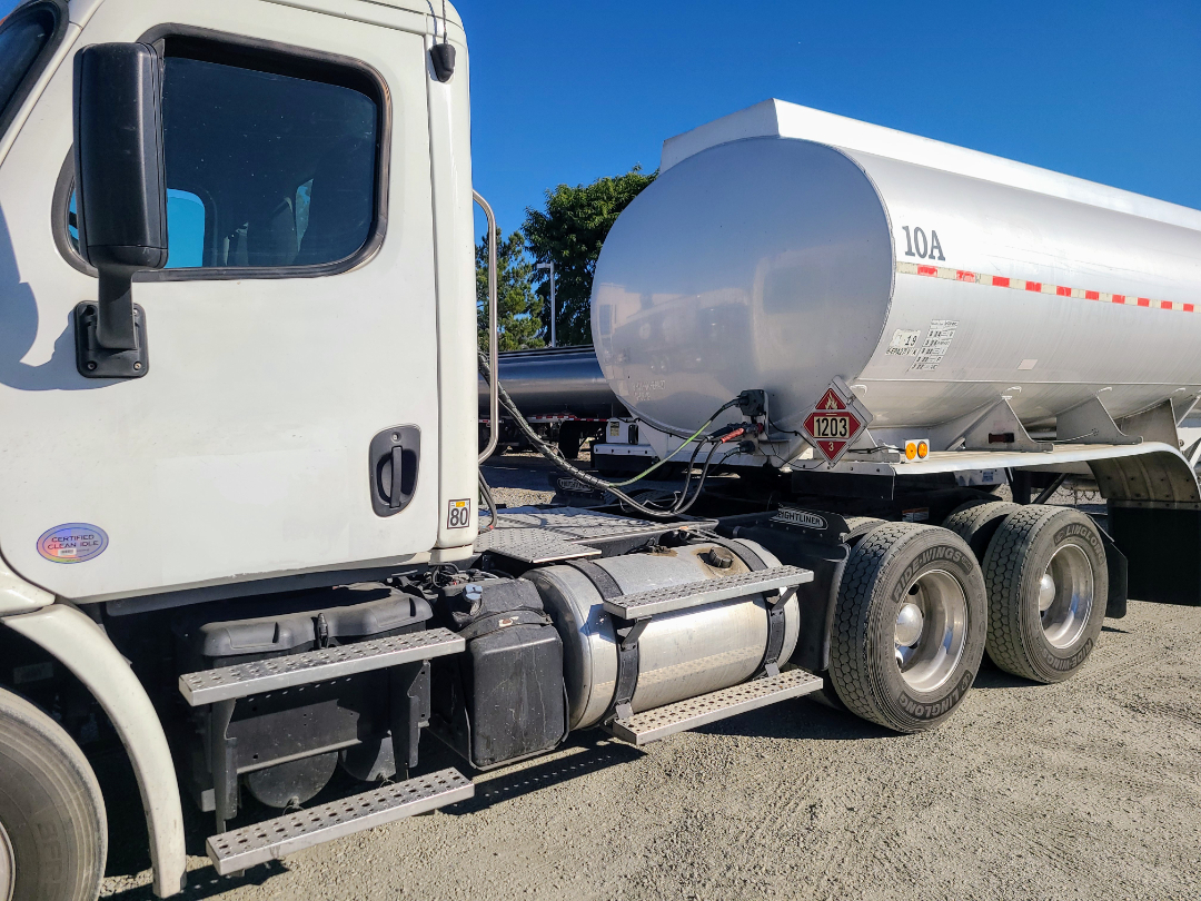 Beall semi truck with a cylindrical tanker trailer showing dual rear axles and fuel tank; visible hazard placard 1203 and 10A markings on tanker.