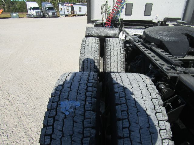 Kenworth T680 chassis area showing dual rear tires and cab connection; gravel lot in background.