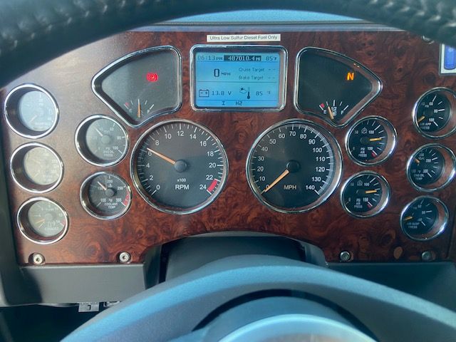 Dashboard of a 2015 Mack CXU613 showing multiple gauges, a central digital display, and wood-grain trim. The digital screen reads maintenance and fuel info with various icons; surrounding gauges include RPM and MPH dials.