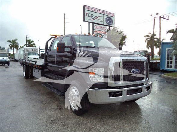 Ford F-750 tow truck front three-quarter view showing extended cab and flatbed, chrome front bumper, black body, and Ford grille.