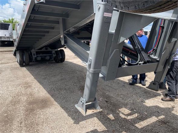 Trailer undercarriage with tandem axles and support leg, grey metal frame, hydraulic lines visible.