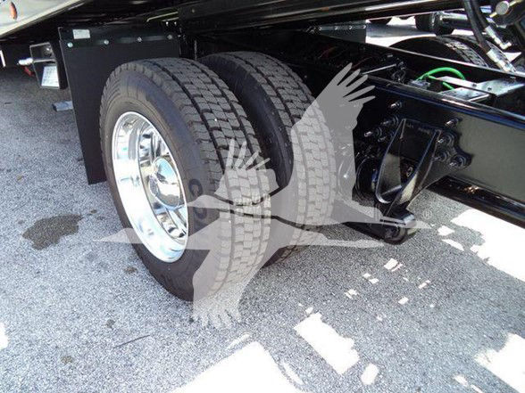 Tow truck rear dual wheels on axle with black chassis and chrome rims, visible suspension and tires.