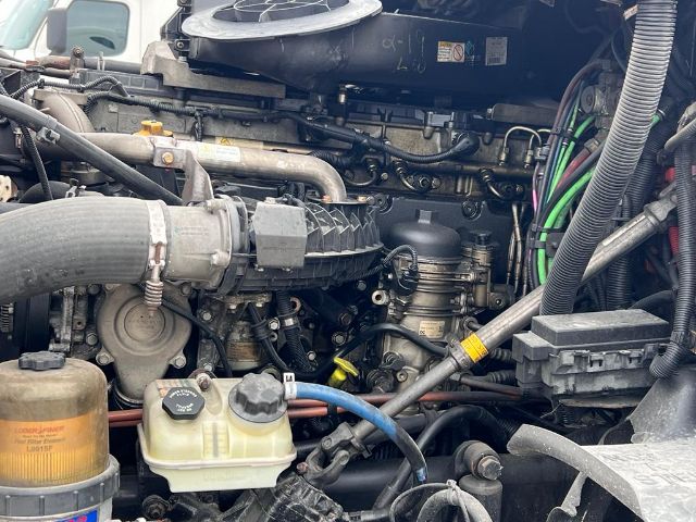 Cascadia truck engine bay with hoses, reservoirs, and belts visible; sensors and wiring loom present.