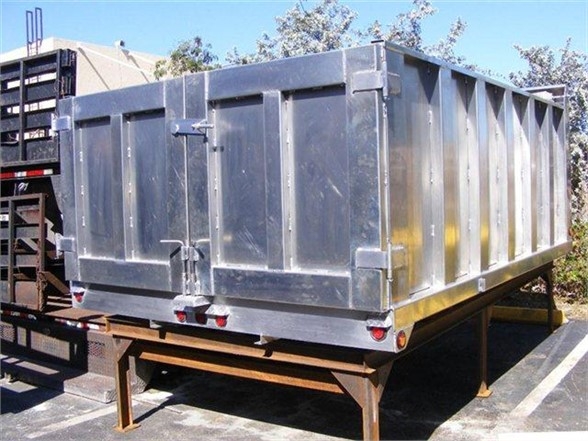 Steel dump body in a truck bed on a stand, rear doors with latches, metal panels and hinges visible.
