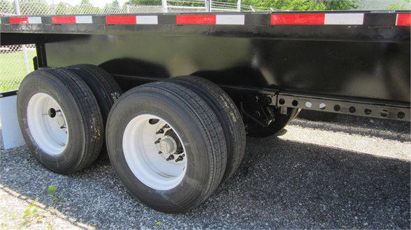 Flatbed trailer axle area with dual rear wheels and black extendable deck undercarriage.
