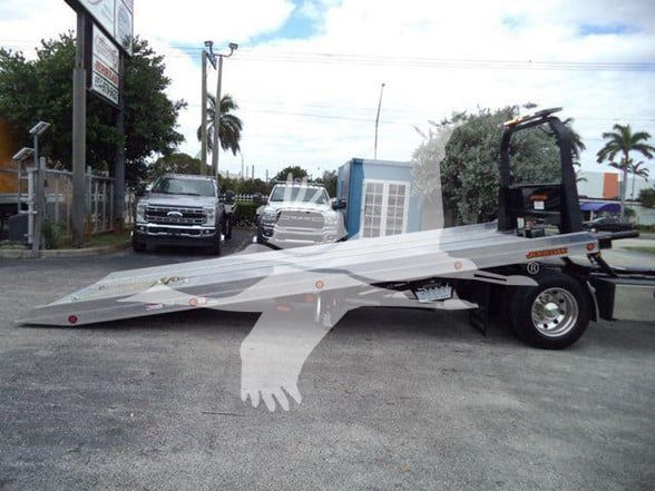 Freightliner Business Class M2 106 with a long flatbed tow setup and wheel lift, side view showing chrome wheels and cab area.
