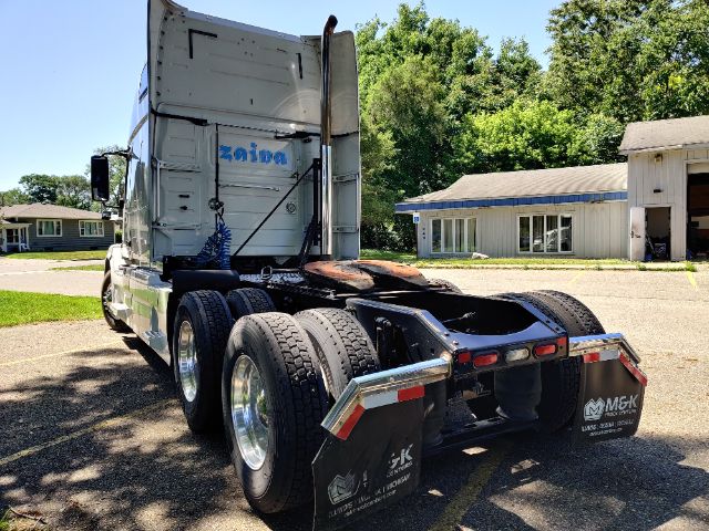 Volvo 670 tractor rear view showing triple axle and fifth wheel; mud flaps with MGK branding; surrounding rural lot.
