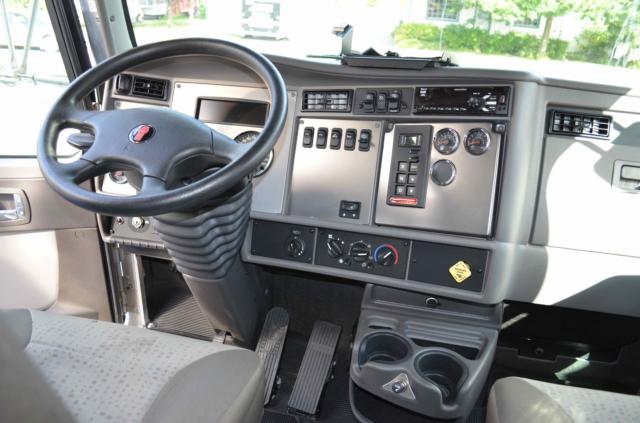 Kenworth T370 interior dashboard view showing steering wheel, control panels, gauges, and cup holders.