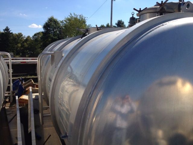 Vacuum tank trailer with polished stainless cylindrical tanks and metal railing visible from side view.