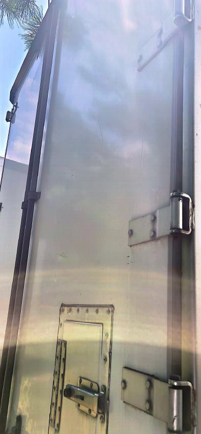 Utility trailer door and hinges with latch mechanisms visible on a metal panel.