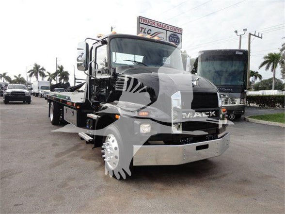 Mack MD6 tow truck in lot with front chrome bumper and tow bed, side mirrors, and palm trees in background.