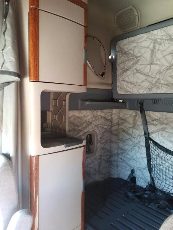 Truck sleeper cab interior with storage cabinets, overhead shelf, and a netted cargo area visible.