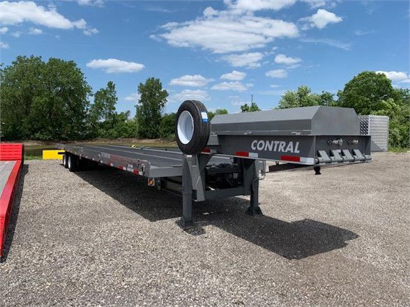 Conrail drop deck container delivery trailer with tandem axles, gray color, flatbed undercarriage, spare tire mounted near the front, clear sky.
