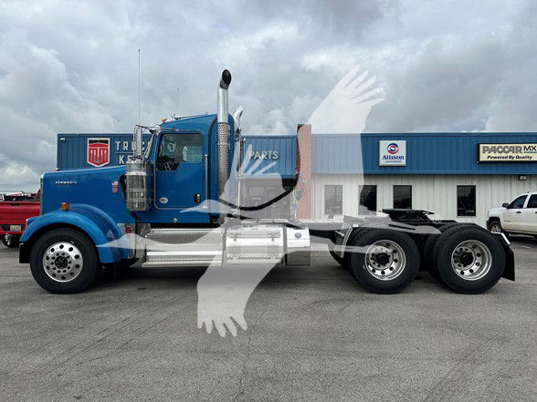 Kenworth W900L tractor cab in blue, side profile showing chrome fuel tanks and dual rear axles.