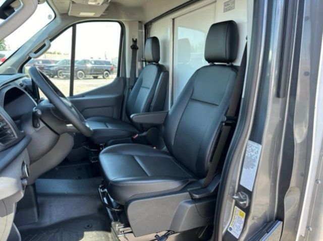 Ford Transit 350 interior showing front driver and passenger seats in black leather/sony vinyl with steering wheel and dashboard visible.